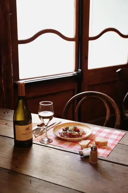 Table dressée près de la fenêtre, bouteille de blanc et assiette du jour